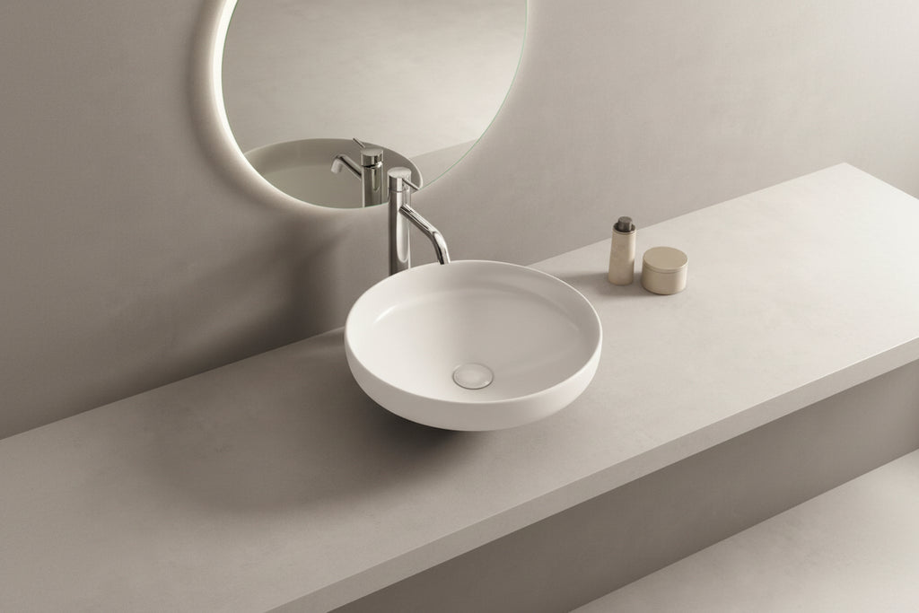 White ceramic sink on a gray concrete countertop with a round mirror above.