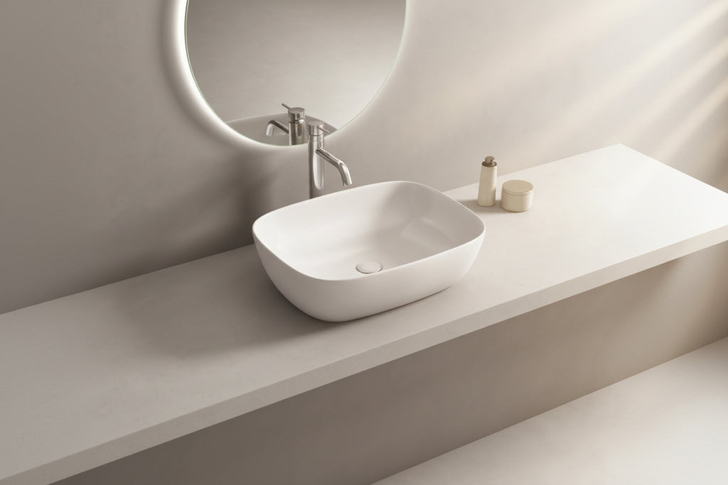 White ceramic sink on a gray countertop with a round mirror above.